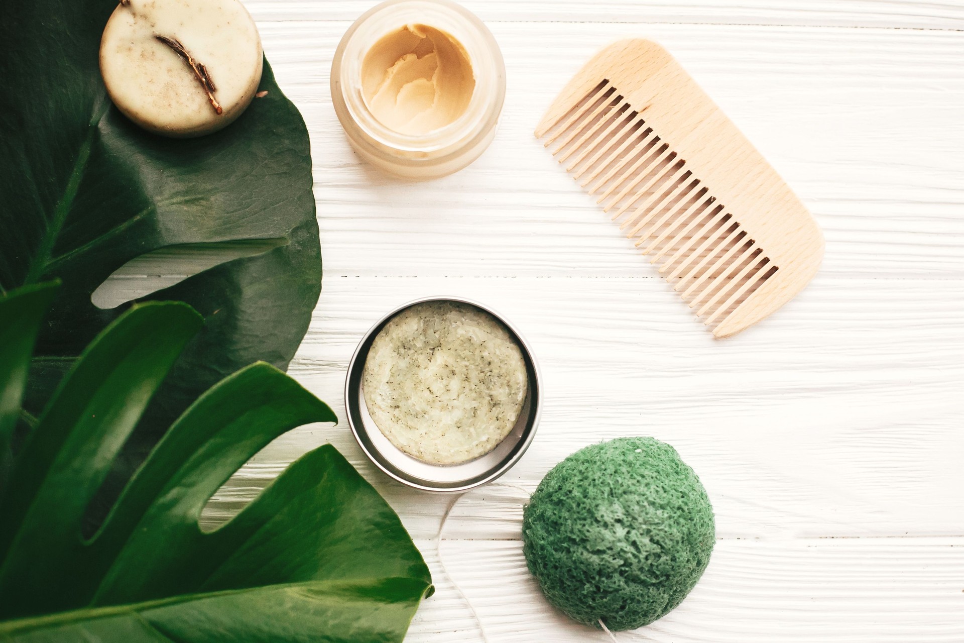 Zero rifiuti piatti laici. Shampoo bar solido ecologico naturale, pennello in legno, balsamo, sapone, spugna konjaku su legno bianco con foglie di monstera verde.  Prodotti eco plastici